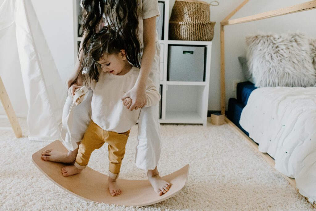 Mother and son enjoy bonding time in a cozy bedroom on a wooden balance board.
