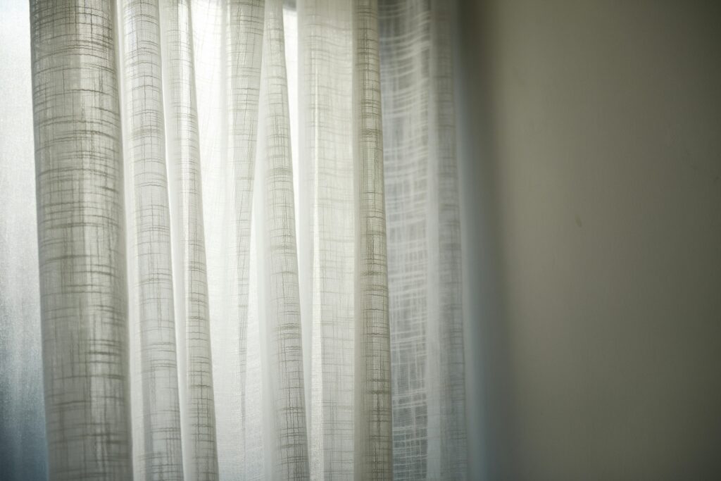 Sheer white curtains gently lit by daylight create subtle shadows on the wall.